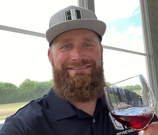 A glass of estate red held up to the window, with the vineyard and sky behind it.