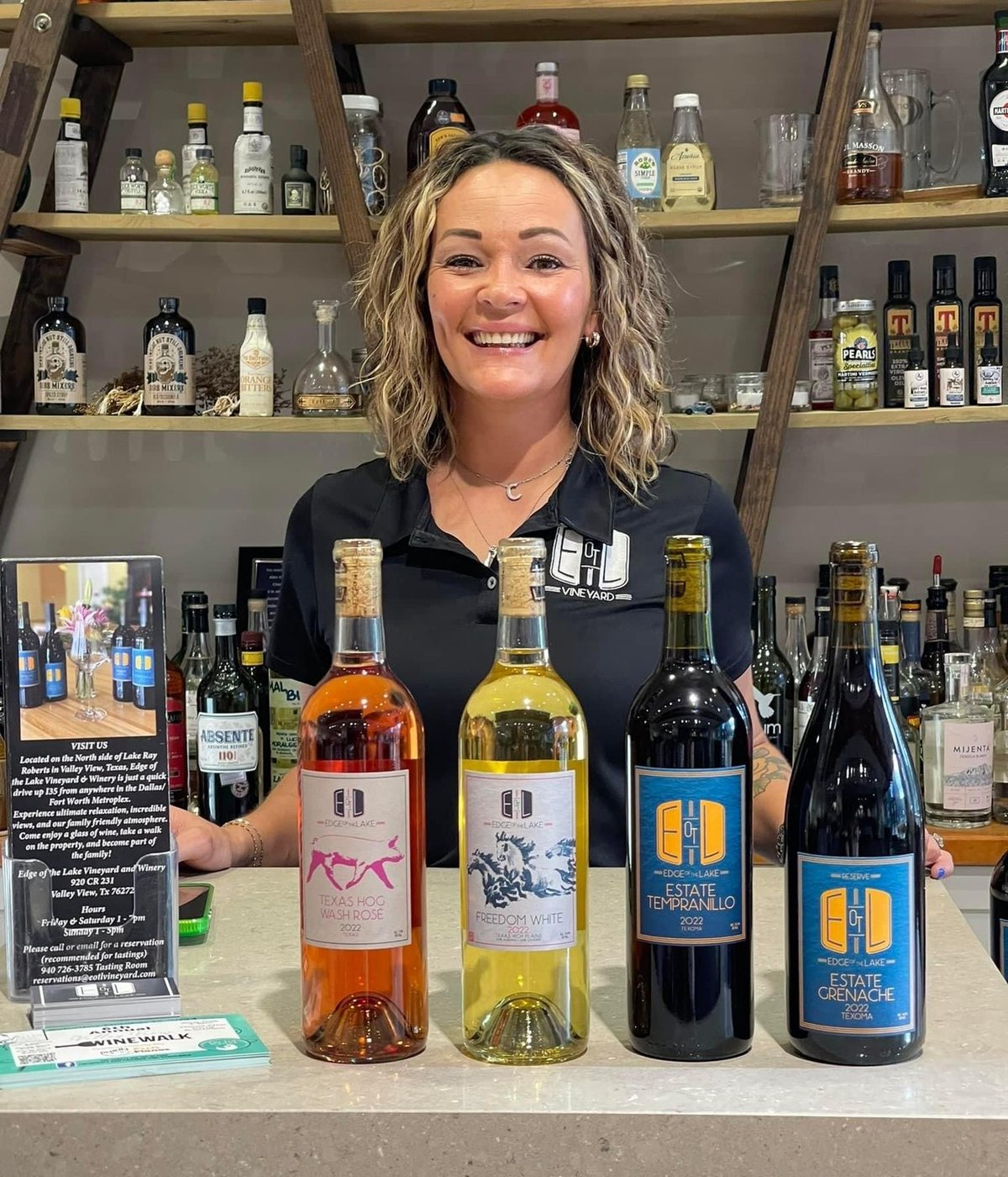 Behind the tasting-room bar with four estate wines lined up: Texas Hog Wash Rosé, Freedom White, Estate Tempranillo, and Estate Grenache.